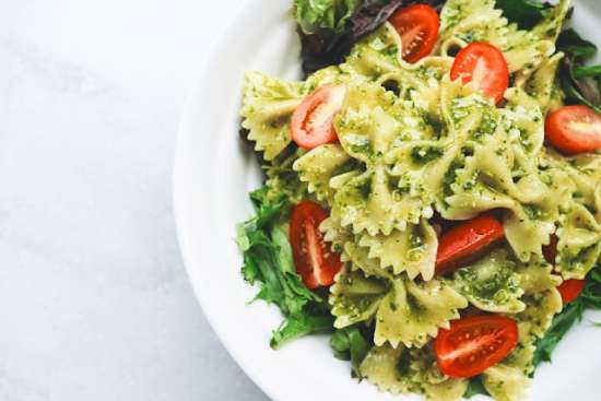 A white plate with pesto pasta and tomatoes