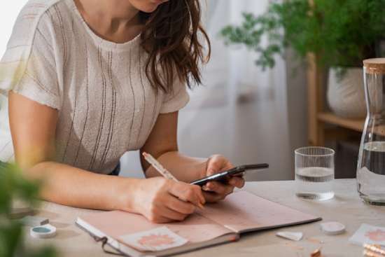  A woman looking at her phone and writing down plans in her calendar so she is prepared for the Sabbath 