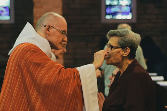 A woman kneeling and receiving communion from a priest at a Catholic Church on Sunday
