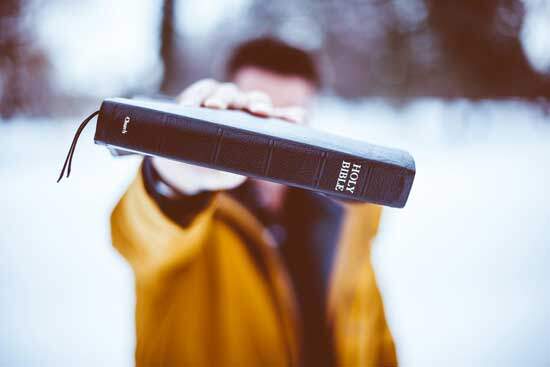 A man in a snowy forest holds out a copy of the Holy Bible.