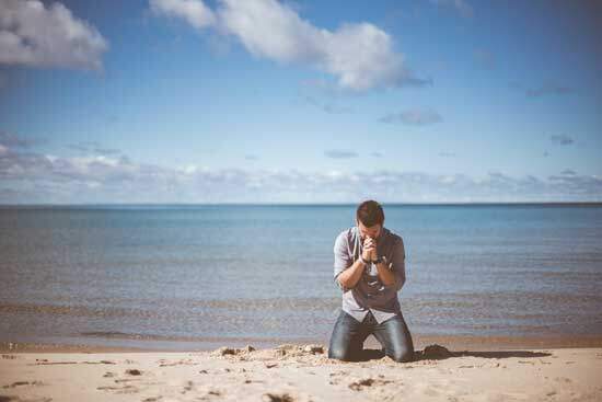 Man kneeling in prayer at seashore as he seeks to have relationship with Jesus & walk in obedience to His will by Holy Spirit