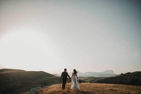 A newly married couple holding hands and walking in the sunset