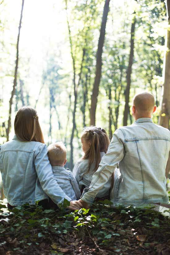 Father, mother, son & daughter sitting on the ground in a forest. Parents holding hands together in love & commitment