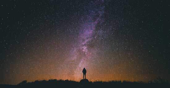 A silhouette of a man standing under a vast, starry sky