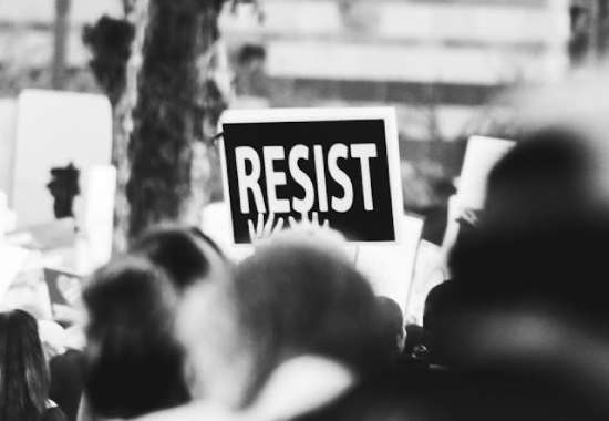 Hands holding a sign that says, Resist