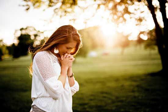 A woman bowing her head in prayer and clasping her hands as she prays to God for salvation