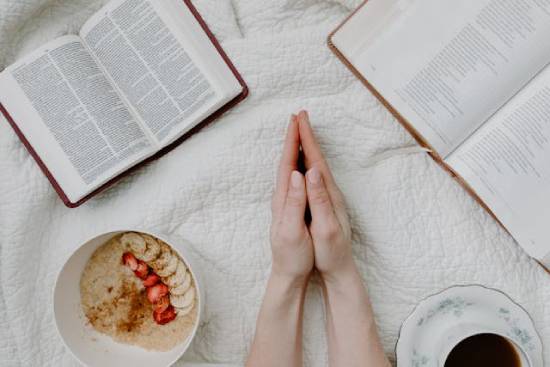 The folded hands of a woman surrounded by two open Bibles, a bowl of oatmeal, and a cup of tea A woman's hands are folded while surrounded by Bibles, a bowl of oatmeal, and a cup of tea. This illustrates how faith is a lifestyle that's shaped by God's Word and the Holy Spirit.
