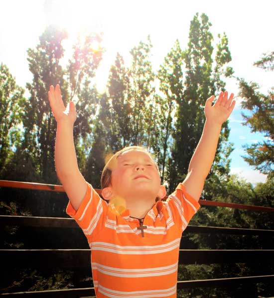 Young boy raising his hands toward heaven and prays with closed eyes, as we study that angels bear our prayers to heaven