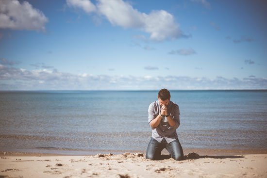 A man kneeling in prayer on the seashore and crying out to God with a broken heart