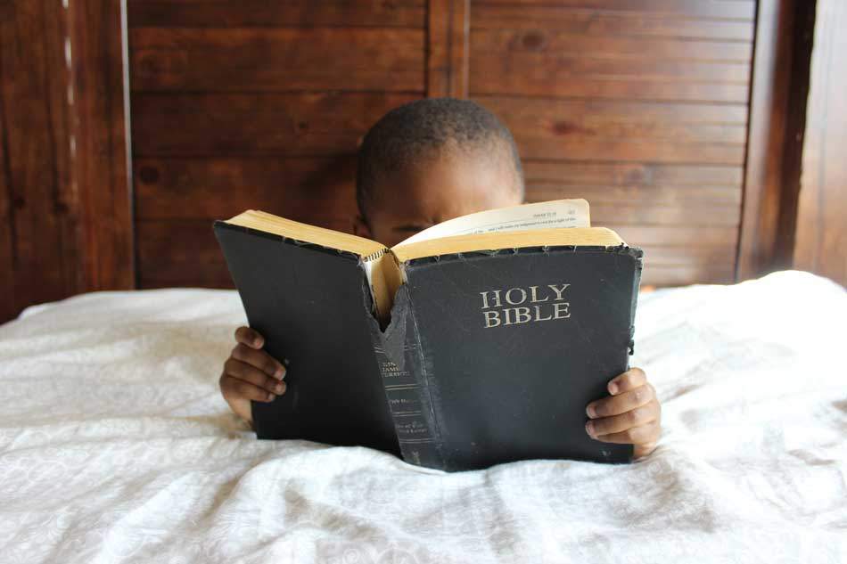 A young child reading the Holy Bible intentively and with much interest - AAAF