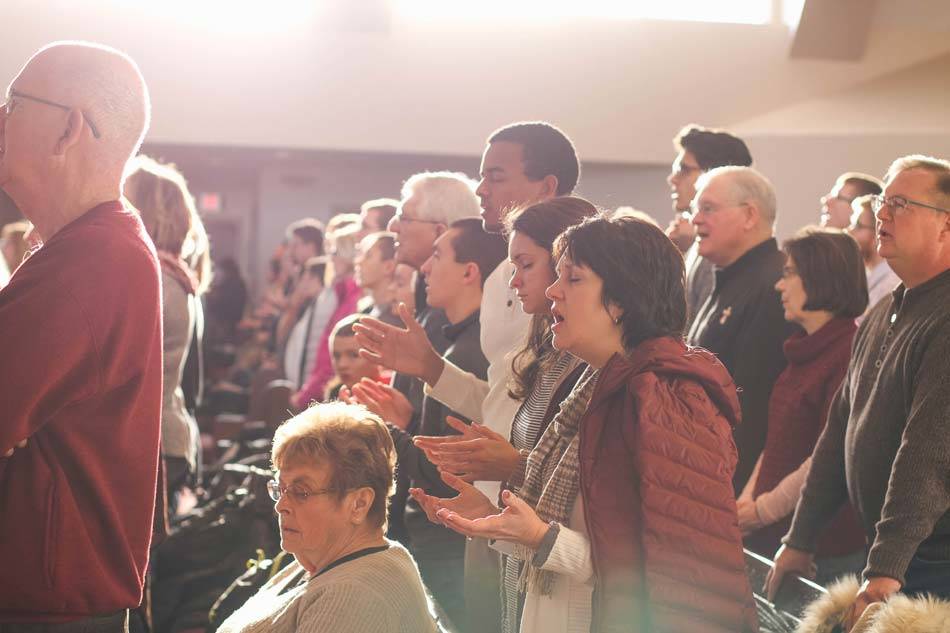 Church Congregation standing from their pews & singing Amen during worship with closed eyes and open hands - AAAF