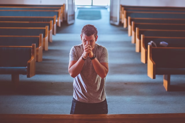 Man kneeling before a Church alter and praying earnestly as we learn from Jesus to be humble and find rest in Him.