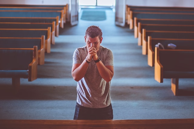 Man praying at the altar of a Church with empty pews in the background as we learn true prophets bring people back to God.