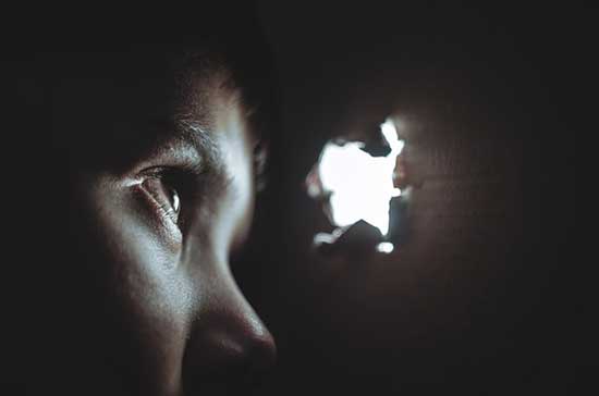 Boy in a dark room, looking through a hole towards the light, as we explore how prophecies encourage patience and hope in us.