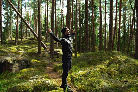 Man stretching his arms in woods as we learn how going out in nature reduces stress level and relaxes our mood.