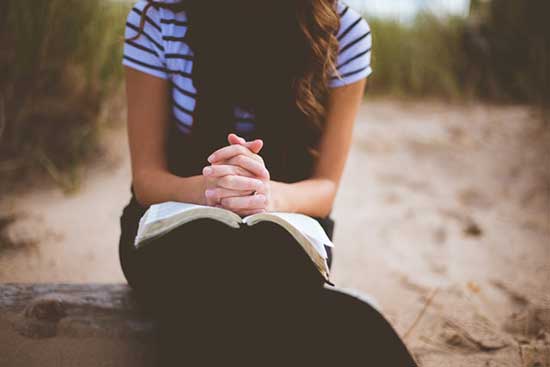 Woman praying with an open Bible as we learn to live worry free, trusting in God's promises from His Holy Word, the Bible.