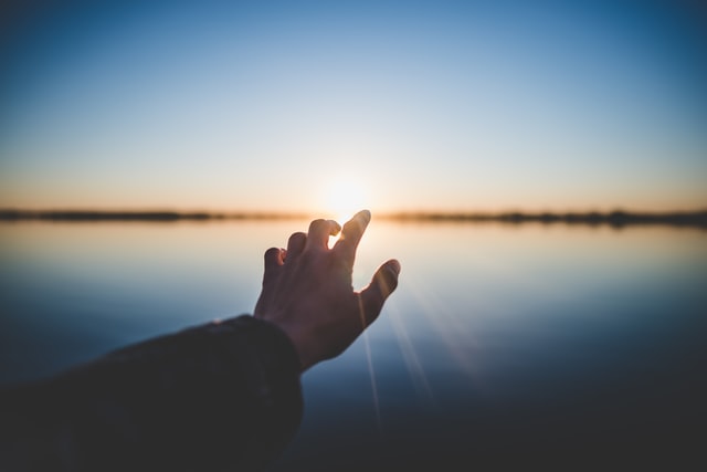 Person's hand reaching out to the sun, as we learn about trusting God in hard times and leaning on His promise of new earth.