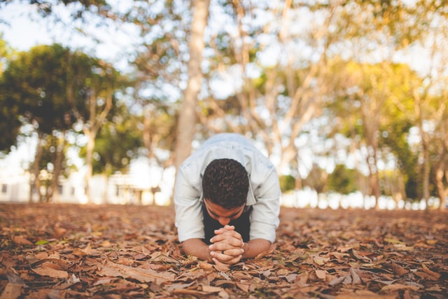 A man kneeling on leaves and praying to God for healing