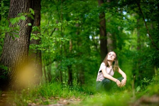 A girl practices forest bathing by sitting surrounded by trees