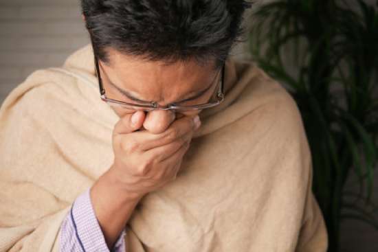 A woman coughing into her hand due to a lowered immune system