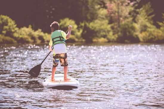 A child riding a paddle board on a lake at summer camp