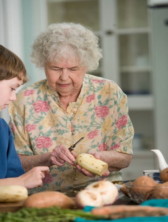 An elderly woman peeling potatoes for a vegetarian meal