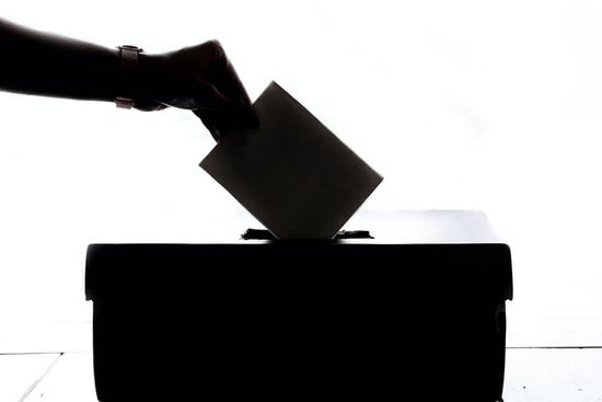 A hand placing a voting ballot in a box at a General Conference session