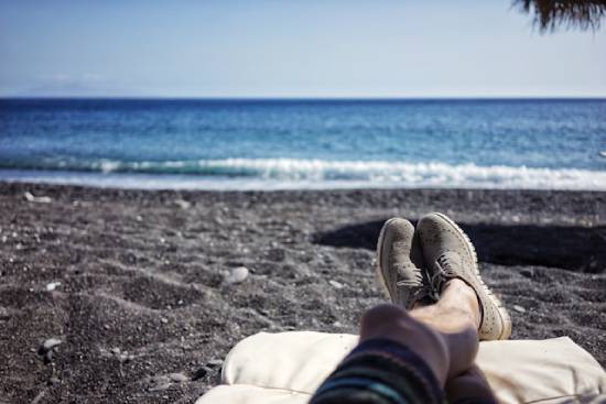 Man putting feet up at the beach A man's laid-out legs can be seen on a lounge chair on the beach in front of an ocean.