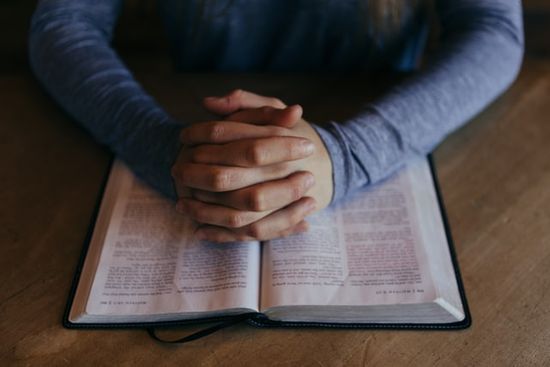 A person with Bible open and hands folded in prayer