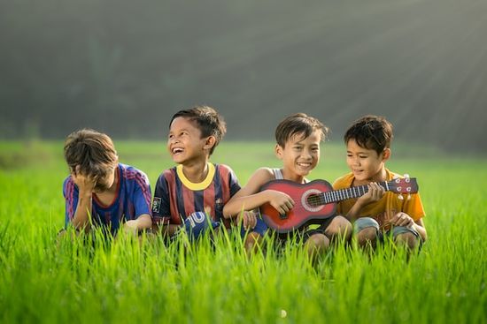 Four boys playing ukulele in a field at summer camp