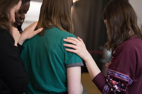 Young women praying with their hands on each other during a Friday night vespers