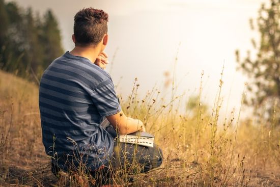 A man sitting in a field and reading the Bible
