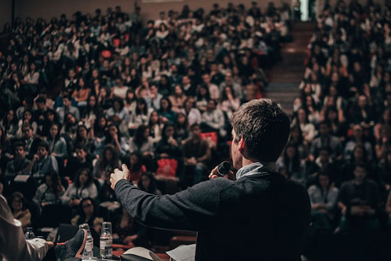 An Adventist preacher speaking to a crowd in an auditorium during an evangelistic meeting