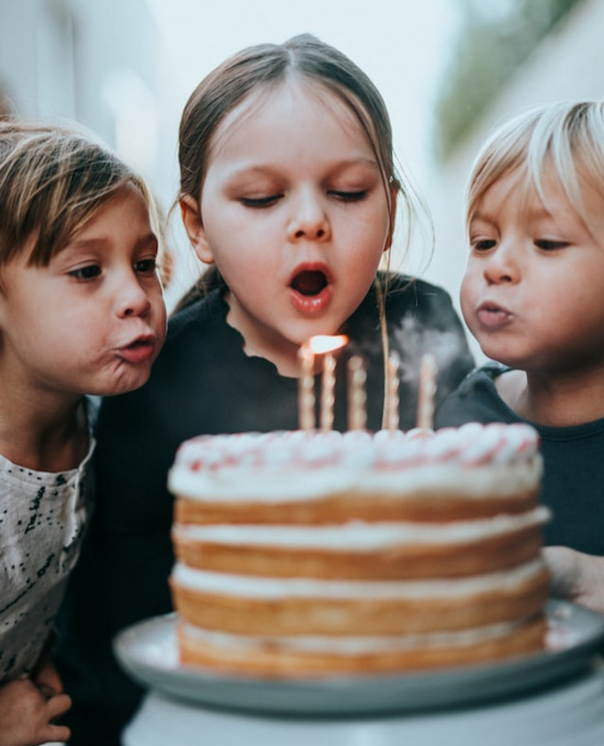 Three children blowing out candles at a birthday party