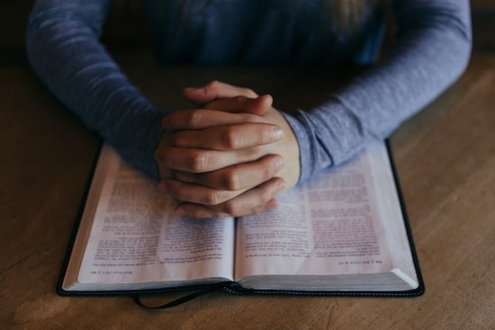 A man's folded hands on an open Bible, studying the Lord's prayer