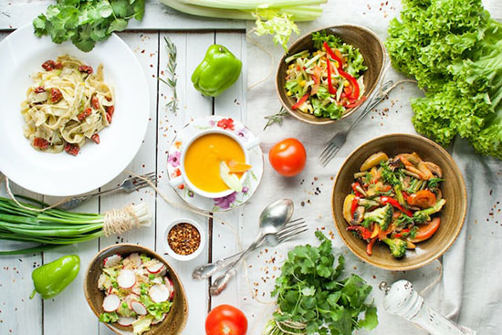 A table with bright green and colorful food that compose a vegetarian diet