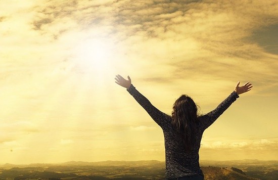 A silhouette of a woman with hands uplifted in a prayer of thanksgiving to God