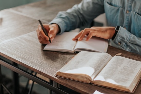 Woman's hands writing in a journal as she studies the doctrines of the Bible