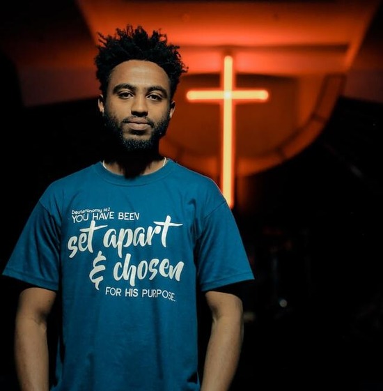 A young adult standing in front of a cross and showing his commitment to follow Jesus Christ