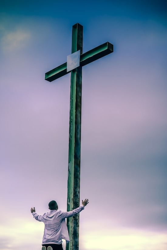 A man kneeling before the cross with arms out in thanksgiving for God's gace