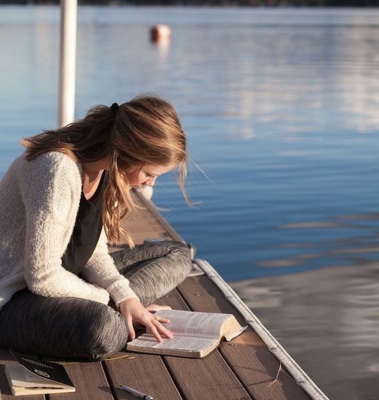 A girl sitting on a dock and reading the Bible to discover God's love