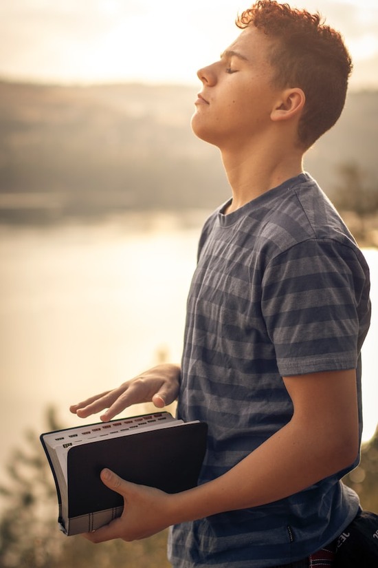 A young man holding a Bible and praying because he has peace through salvation in Jesus Christ