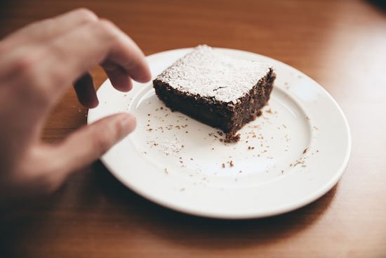 A hand reaching to grab a brownie off a plate in a moment of craving