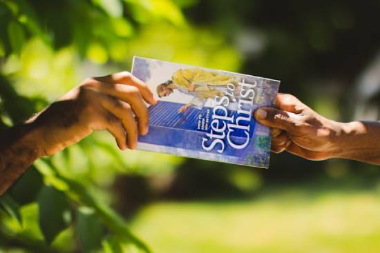 One hand giving a Steps to Christ book to another hand A person hands out a copy of the book