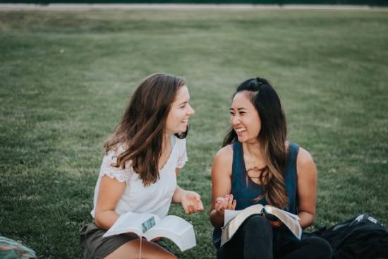Two women studying the Bible outdoors Two young women joyfully study the open Bibles on their laps as they sit on a lawn.