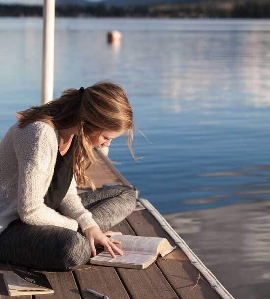 Woman sitting at the shore of a lake, daily feeding on the Word of God, the Bible
