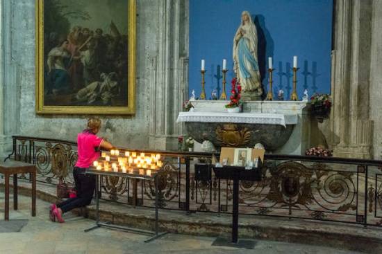 Woman kneeling in prayer in front of candles and a statue of Mary A woman kneels in prayer in front of candles and a statue of Mary, illustrating the third angel's warning against false worship.