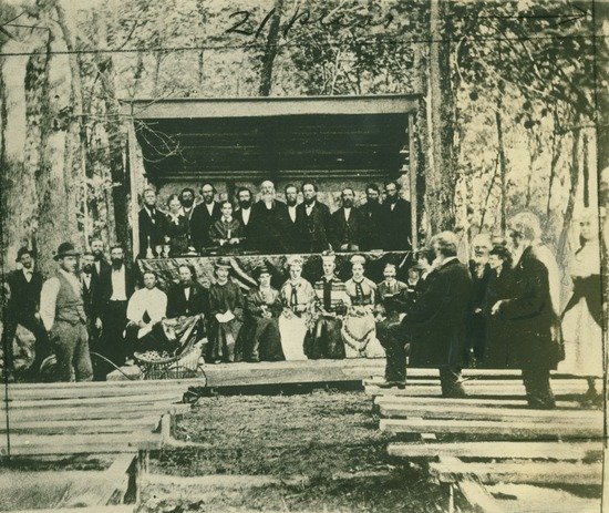 James and Ellen White with other Adventists under a canopy at a camp meeting in 1875