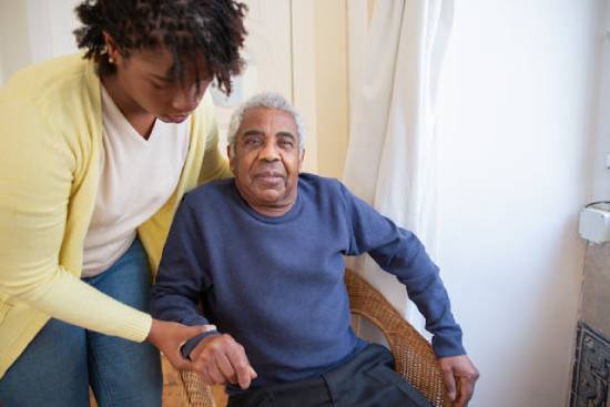 A woman helps an elderly man in a chair, representing how selflessness can help us develop fruits of the Spirit.