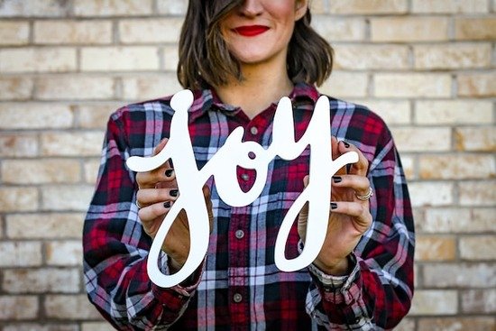 A smiling woman holding up the word joy